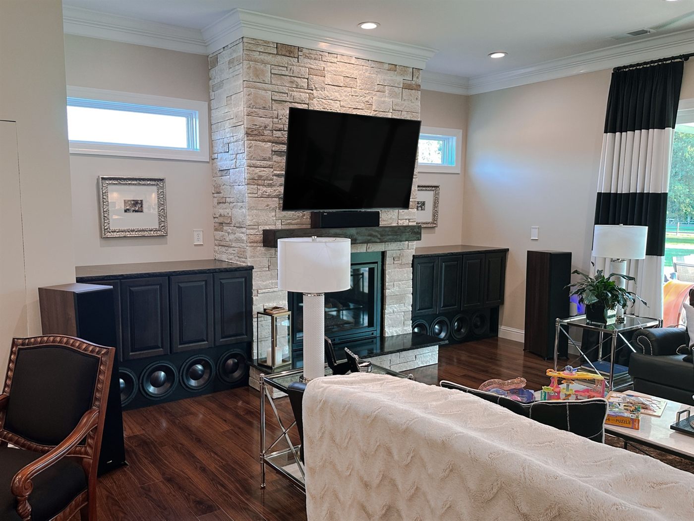 Great room with the TV mounted above a stone fireplace and subwoofers built into the cabinets either side