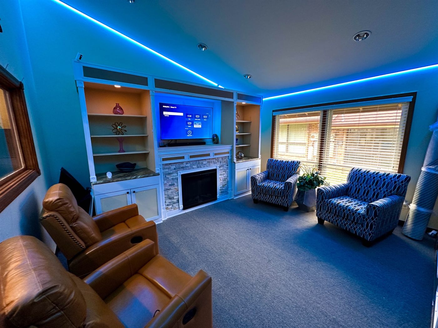 Media room with a wall-mounted TV between built-in shelving, recliners facing the screen, and tunable LED cove lighting around the ceiling