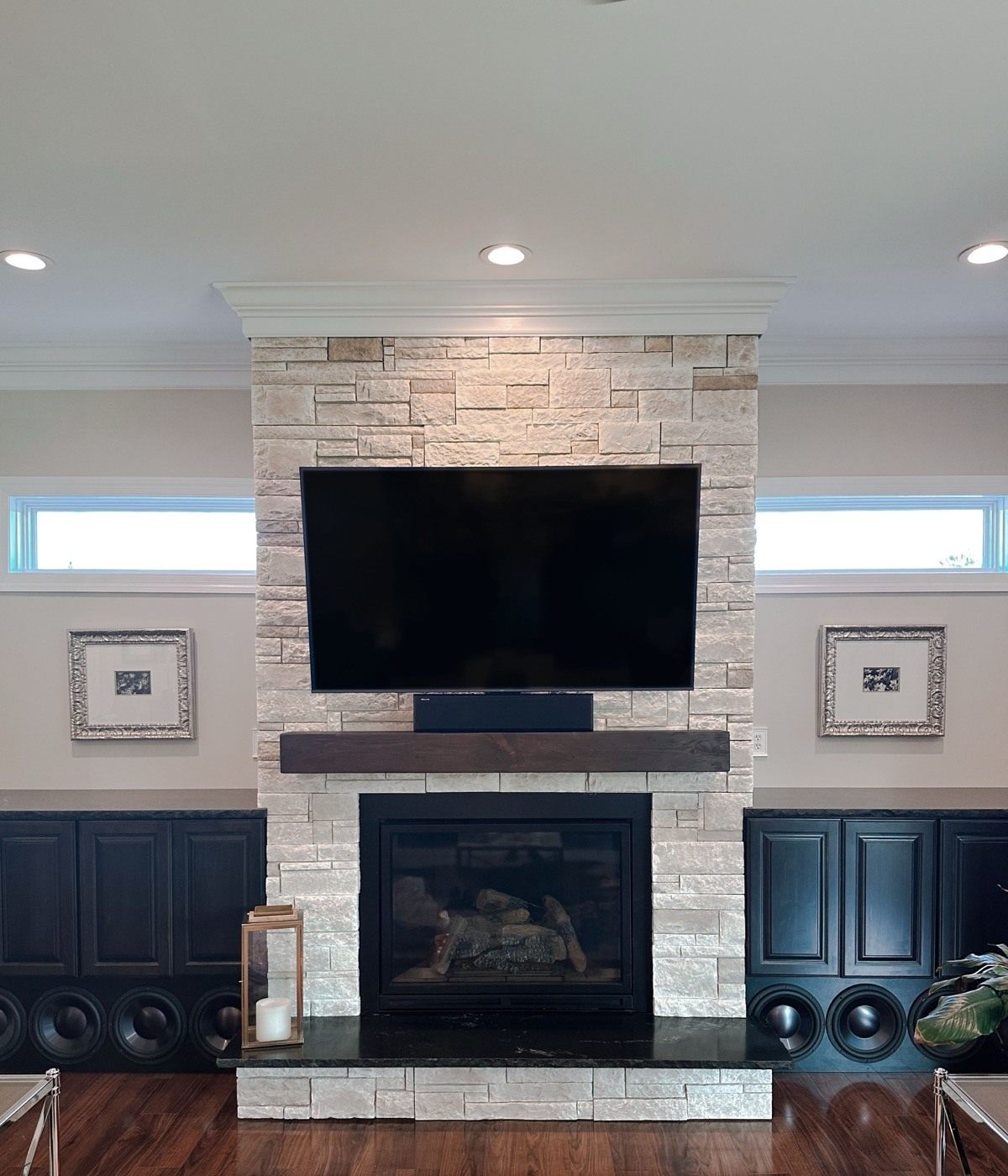 Wildwood great room with a large TV mounted on a stone fireplace above a wood mantel and soundbar