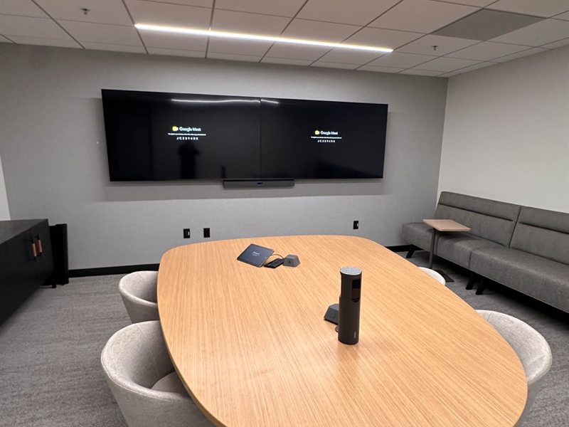 Boardroom with dual wall-mounted displays, a soundbar and an oval conference table