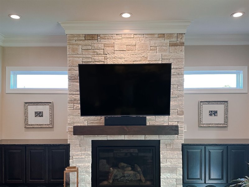 The TV mounted squarely on the stacked stone chimney breast with the soundbar below